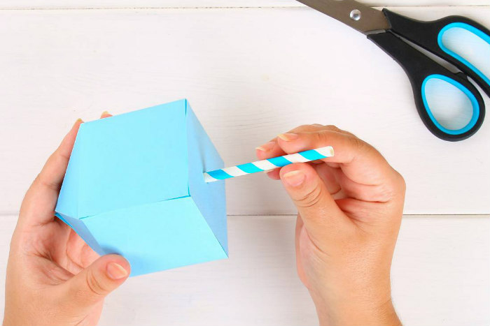 Hands holding a 3D dreidel made of paper and painted light blue with scissors set to the side