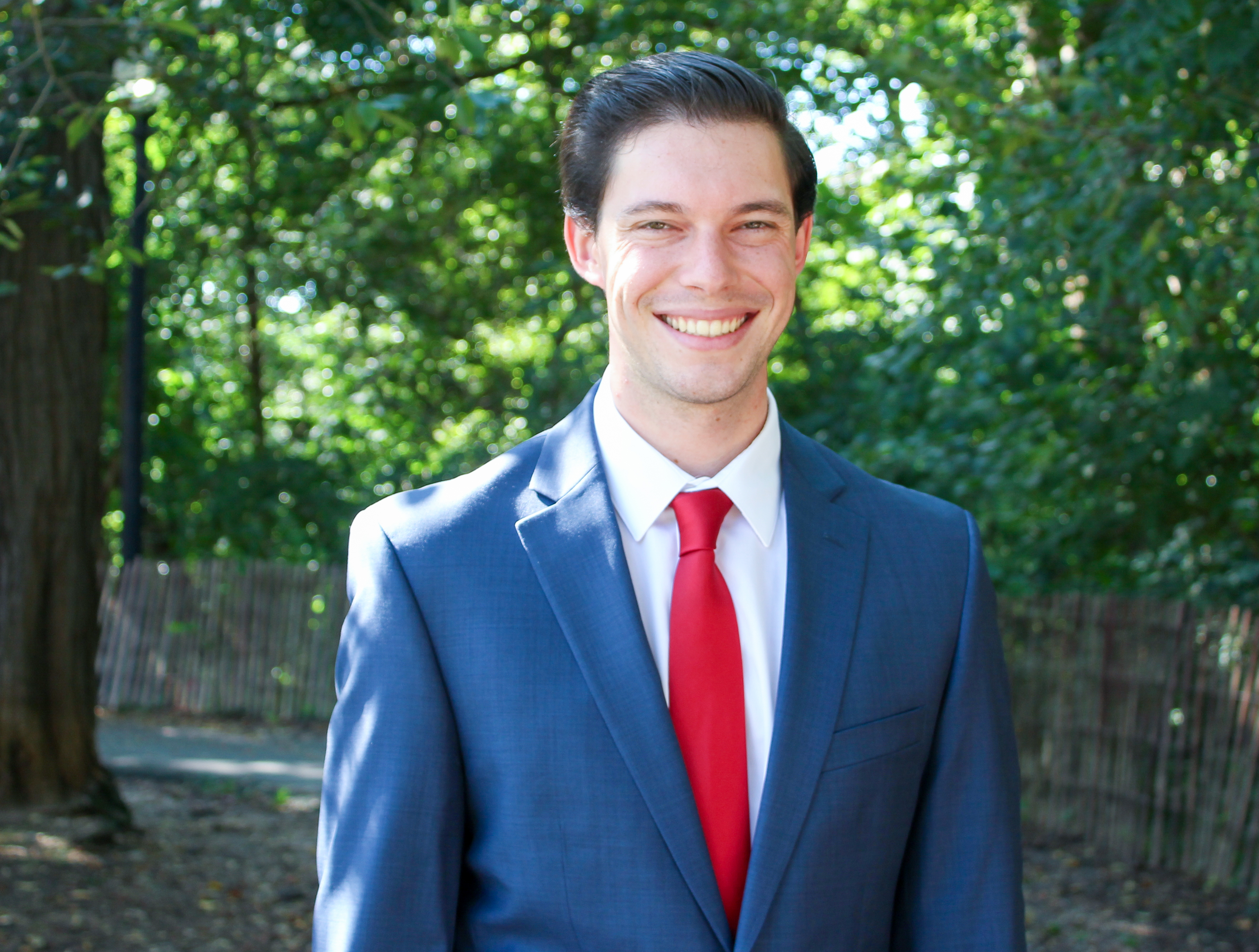 Headshot of Josh Burg wearing a blue suit and a red tie 