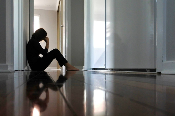 Sad woman sitting on a wooden floor holding her head in her hands as if in grief
