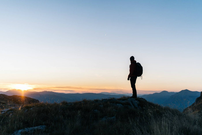 Hiker standing at the top of a peak looking out over nature at sunrise 