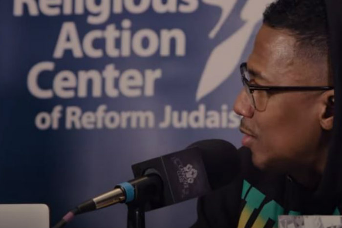 Nick Cannon speaks into a microphone in front of a Religious Action Center banner