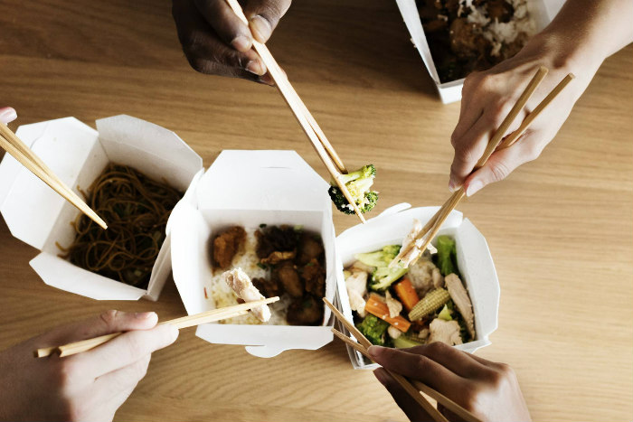 Hands holding chopsticks and digging into carton of Chinese food