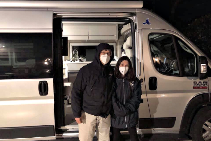 Rabbi Jeff and Mindy Glickman stand together in face masks in front of their white RV