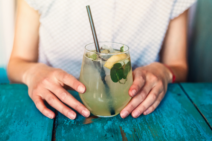 Close up of a womans hands holding a summery beverage with lime and mint