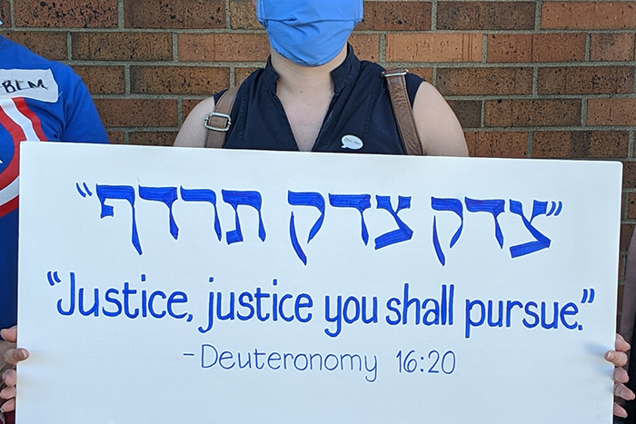 person in mask holding up sign that says Justice Justice You Shall Pursue