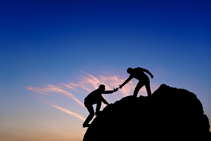 an image of a person helping another person to the top of a mountain