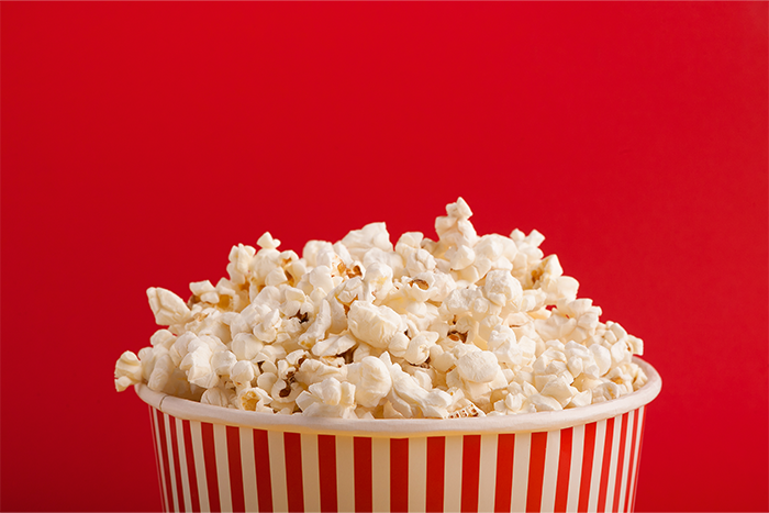 A container of popcorn in front of a red background