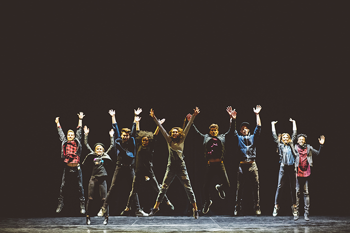 an image of a group of actors with their arms above their heads jumping on a stage