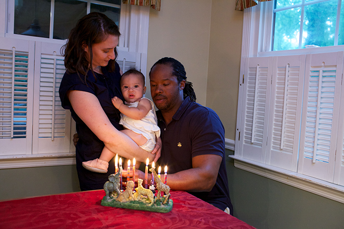 an image of a family with baby sitting at a table with a menorah lite in from of them
