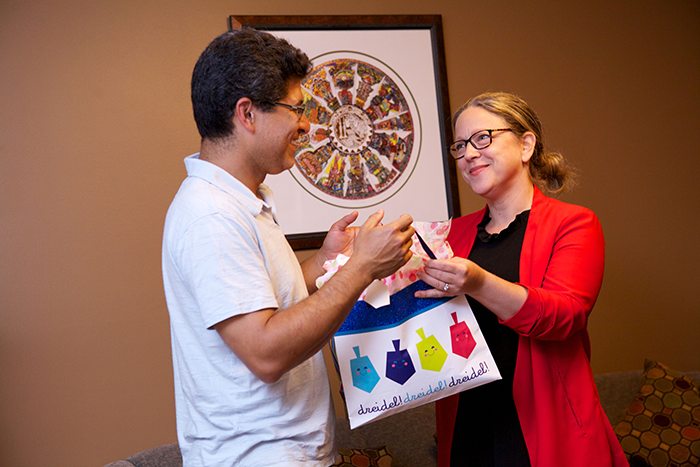 an image of two adults; a woman handing a plastic bag with pictures of dreidals and the word dreidal on it to a man