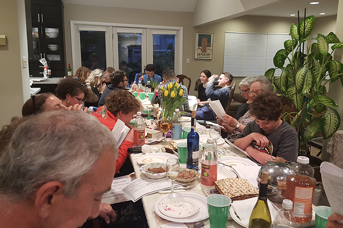 Photo of a group of people sitting around a table, looking at Haggadah on Passover