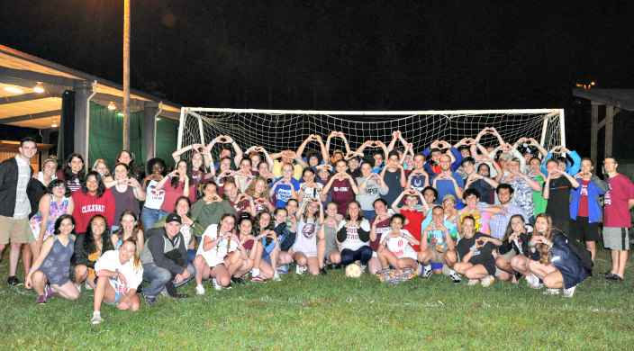 Dozens of campers on a soccer field making a heart shape using their hands 