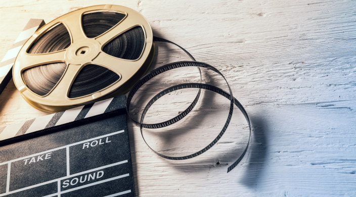 Film reel with clapboard lying on a wooden surface 