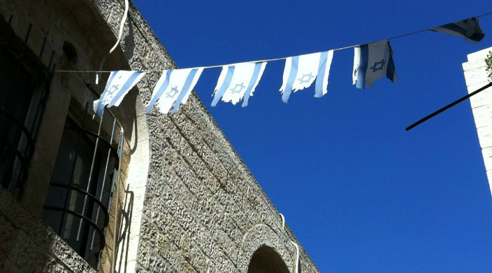 String of tattered Israeli flags hanging between buildings against a blue sky