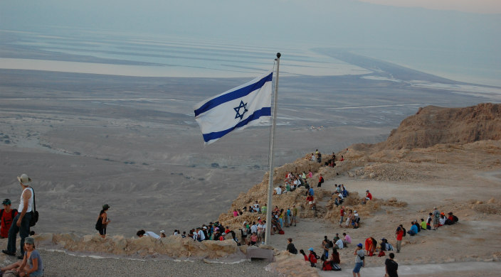 Israeli flag on flagpole in desert, populated by visitors