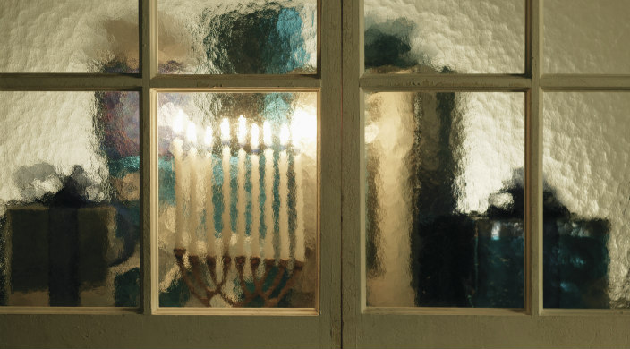 Lit menorah in a window of thick, opaque glass