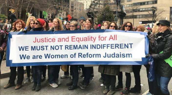 Women march behind a banner that says JUSTICE AND EQUALITTY FOR ALL