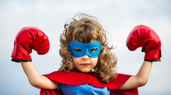 Young girl with blonde curls dressed in superhero costume with mask and boxing gloves