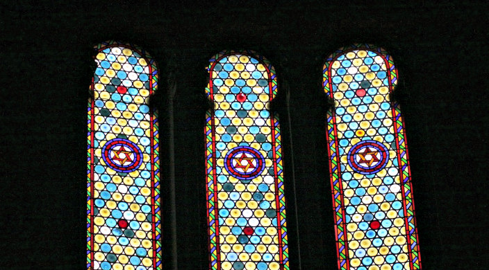 Three stained glass windows bearing Stars of David against an all black background