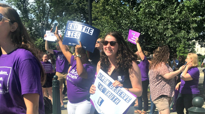 Activist woman protesting outside the Supreme Court in purple shirts carry pro choice signs 