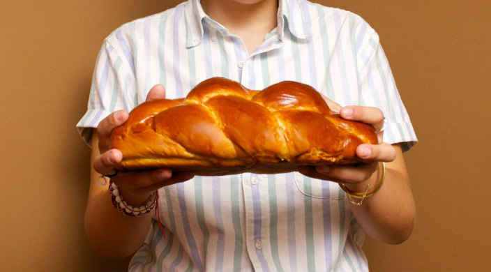 Close up of hands holding a loaf of challah against a striped shirt 
