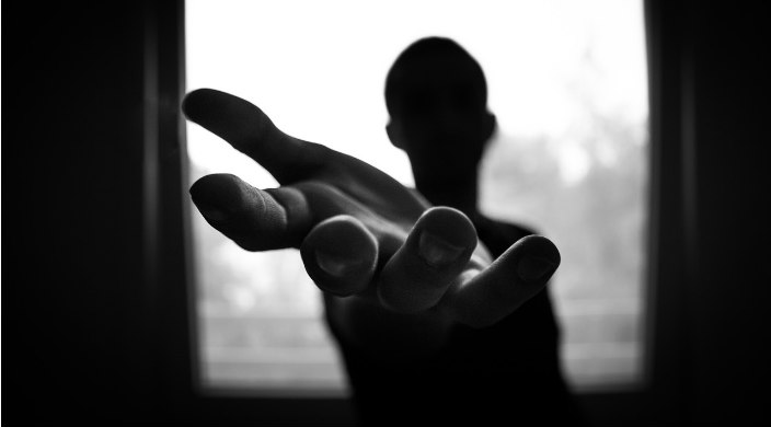 Black and white photo of a man's hand reaching out from the darkness