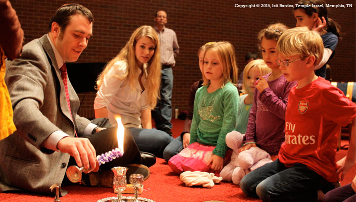 A rabbi with children dipping the Havdalah candle into a cup of wine