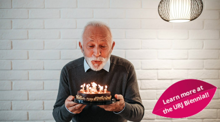 White-haired man holding a birthday cake and blowing out the candles on it