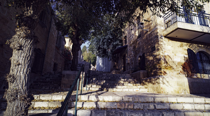 Corner of a building and a flight of stairs along a tree-lined alleyway in Jerusalem's Old City