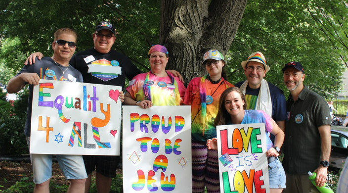 Individuals dressed in rainbow clothing and holding Jewish signs at a Pride rally
