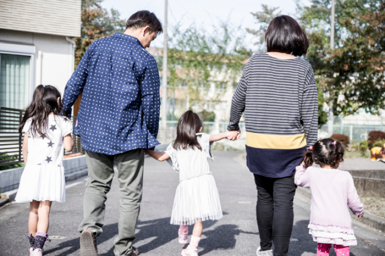 an image of a family with two parents and two young children walking and holding hands