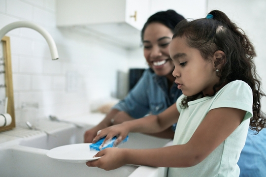 mother teaching child to wash dishes