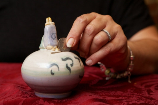 Hand dropping a coin into a ceramic tzedakah box