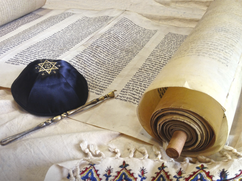 A torah scroll opened next to a blue yarmulke with a gold Star of David design