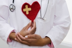 A person wearing a doctor's coat and holding a heart made of felt 