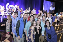 Large group of happy NFTY teens posing in front of the stage where a band is playing