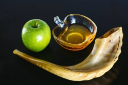Shofar with a green apple and a bowl of honey on a black background