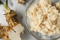 Apple horseradish in a clear bowl with raw horseradish root lying next to it 