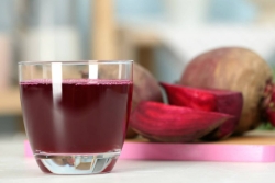 Purpleish Hanukkah cocktail in a short glass with sliced beets in the background 