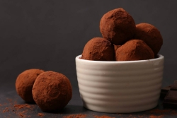 Chocolate truffles in a white bowl with a few lying on the surface next to them