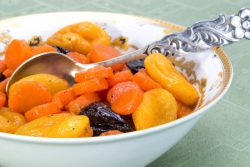 Carrot and prune tzimmes in a white bowl with a silver spoon