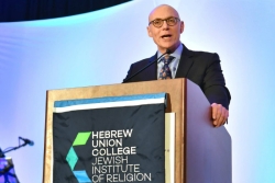 Dr Andrew Rehfeld speaks from a podium with the Hebrew Union College logo on the front