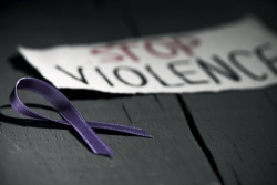 Sign reading STOP VIOLENCE lying on the floor next to a purple domestic violence awareness ribbon