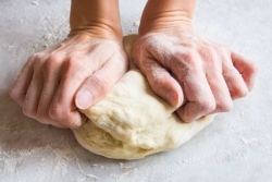 Hands kneading a ball of dough on a white surface
