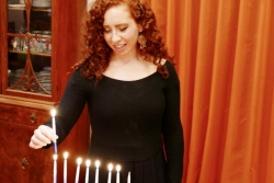 Redheaded young woman lighting a full Hanukkah menorah 