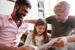 Two dads reading a book with their young daughter