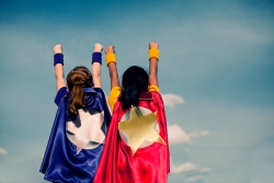Two young girls facing forward wearing superhero capes 