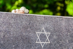Closeup of a headstone with a Star of David engraving and small stones set on top 