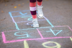 Childs feet in white shoes and striped socks jumping on a chalked hopscotch board