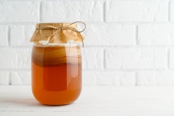 Mason jar of homemade kombucha tea against a white brick wall 